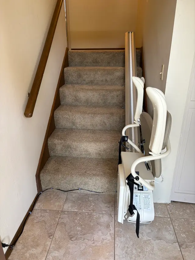 Harmar stair lift with its seat folded at the foot of a carpeted staircase, installed by Peak Pro