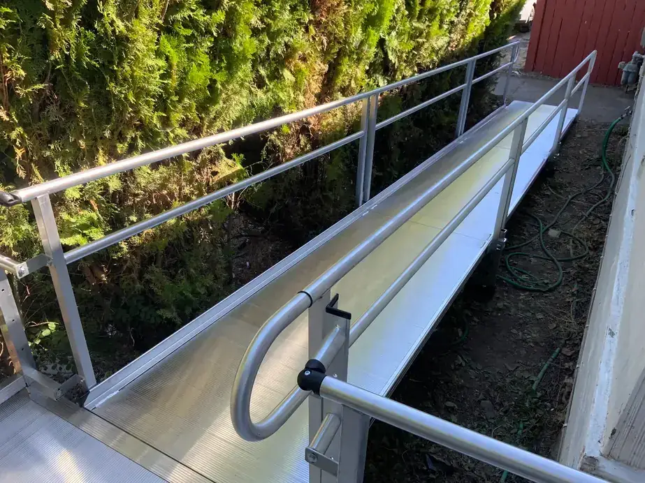 Peak Pro aluminum ramp with handrails and a top platform beside a hedge