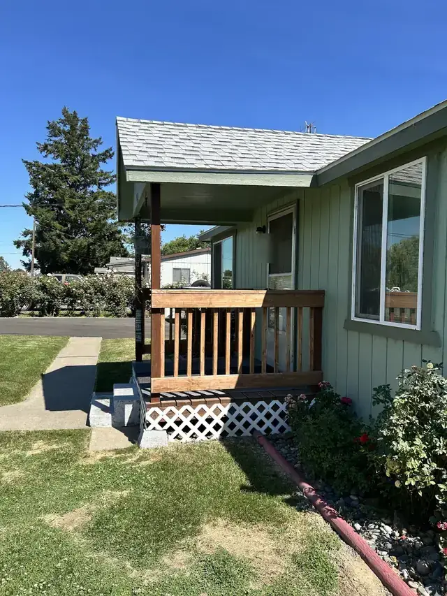 New covered porch with a stained wood rail, lattice skirt and concrete steps on a green-sided Yakima home