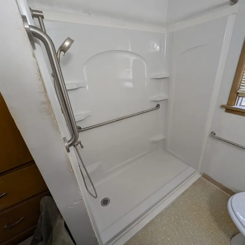 White walk-in shower with grab bars and a hand shower installed by Peak Pro