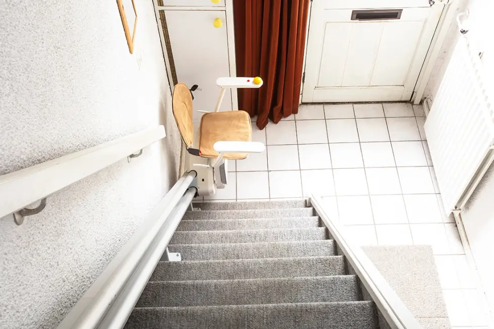 Stair lift with its seat parked at the top of a carpeted staircase in a Yakima home, installed by Peak Pro