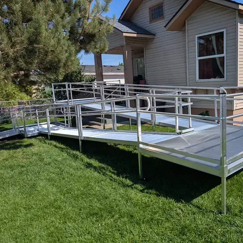 Modular aluminum ramp with platforms and handrails crossing a lawn beside a beige house, built by Peak Pro